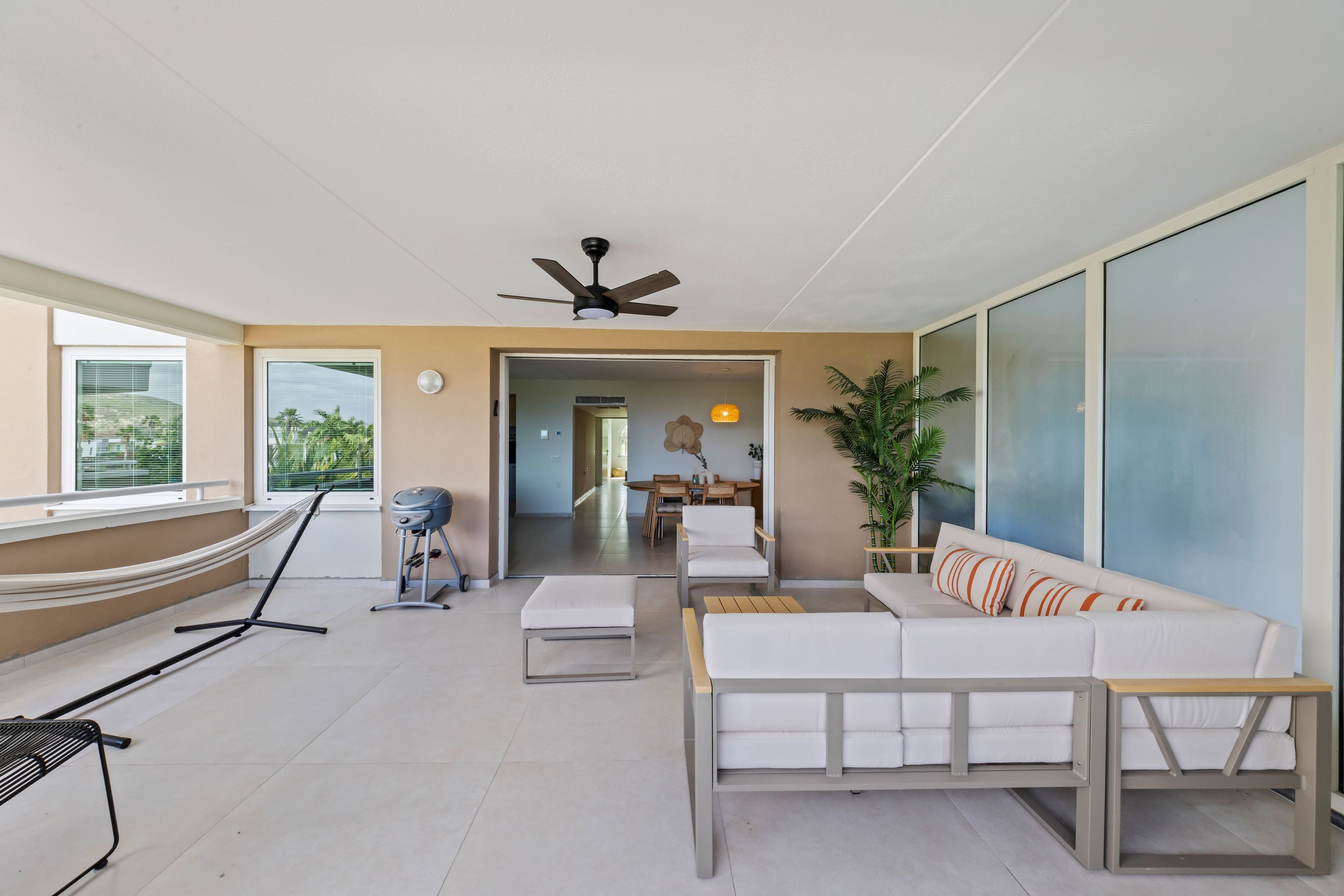 Uma sala de estar moderna com um sofá, uma rede, um ventilador de teto e vista para o exterior.