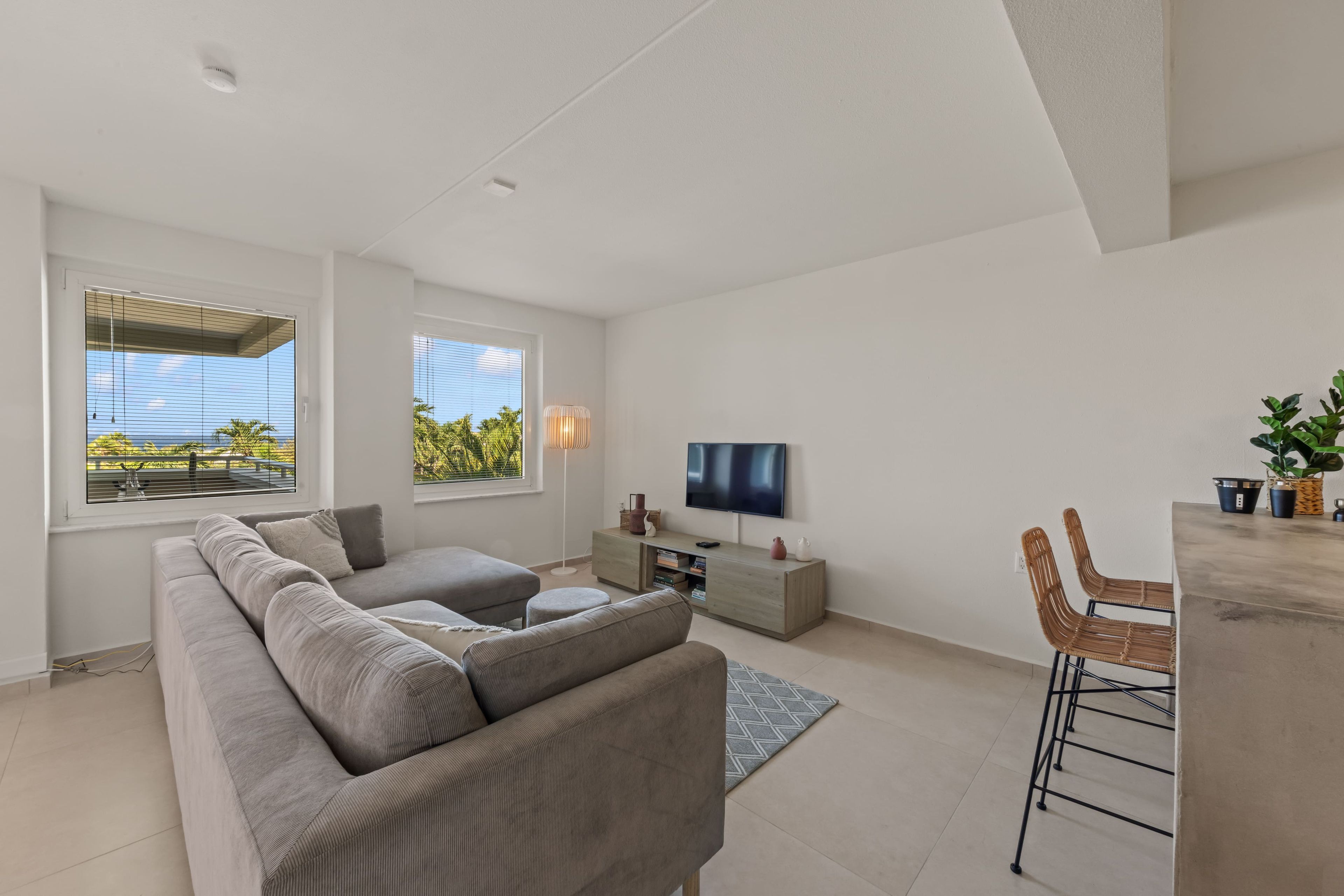 A modern living room with a sectional sofa, a flat-screen TV, and a dining area with a bar stool.