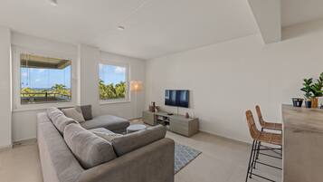 A modern living room with a sectional sofa, a flat-screen TV, and a dining area with a bar stool.