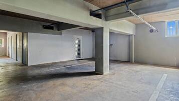 Un vaste espace intérieur inachevé, avec des piliers en béton, une porte portant l’inscription « BUREAU » et des tuyaux apparents au plafond.