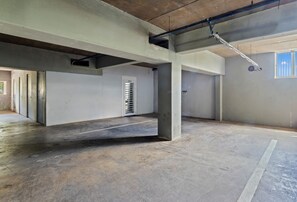Ein großzügiger, unvollendeter Innenraum mit Betonsäulen, einer Tür mit der Aufschrift 'OFFICE' und freiliegenden Leitungen an der Decke.