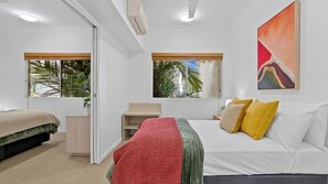 A bedroom with a bed, bedside table, and a window with a view of palm trees. - Two Bedroom Resort Apartment Near Four Mile Beach | Ivy Pearl Apartment (Port Douglas)