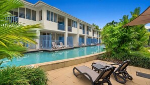 A hotel with a swimming pool, lounge chairs, and tropical plants. - Two Bedroom Resort Apartment Near Four Mile Beach | Ivy Pearl Apartment (Port Douglas)