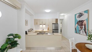A modern kitchen with a central island, stainless steel appliances, and a dining area with a wooden table. - Two Bedroom Resort Apartment Near Four Mile Beach | Ivy Pearl Apartment (Port Douglas)