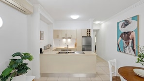 A modern kitchen with a central island, stainless steel appliances, and a dining area with a wooden table. - Two Bedroom Resort Apartment Near Four Mile Beach | Ivy Pearl Apartment (Port Douglas)