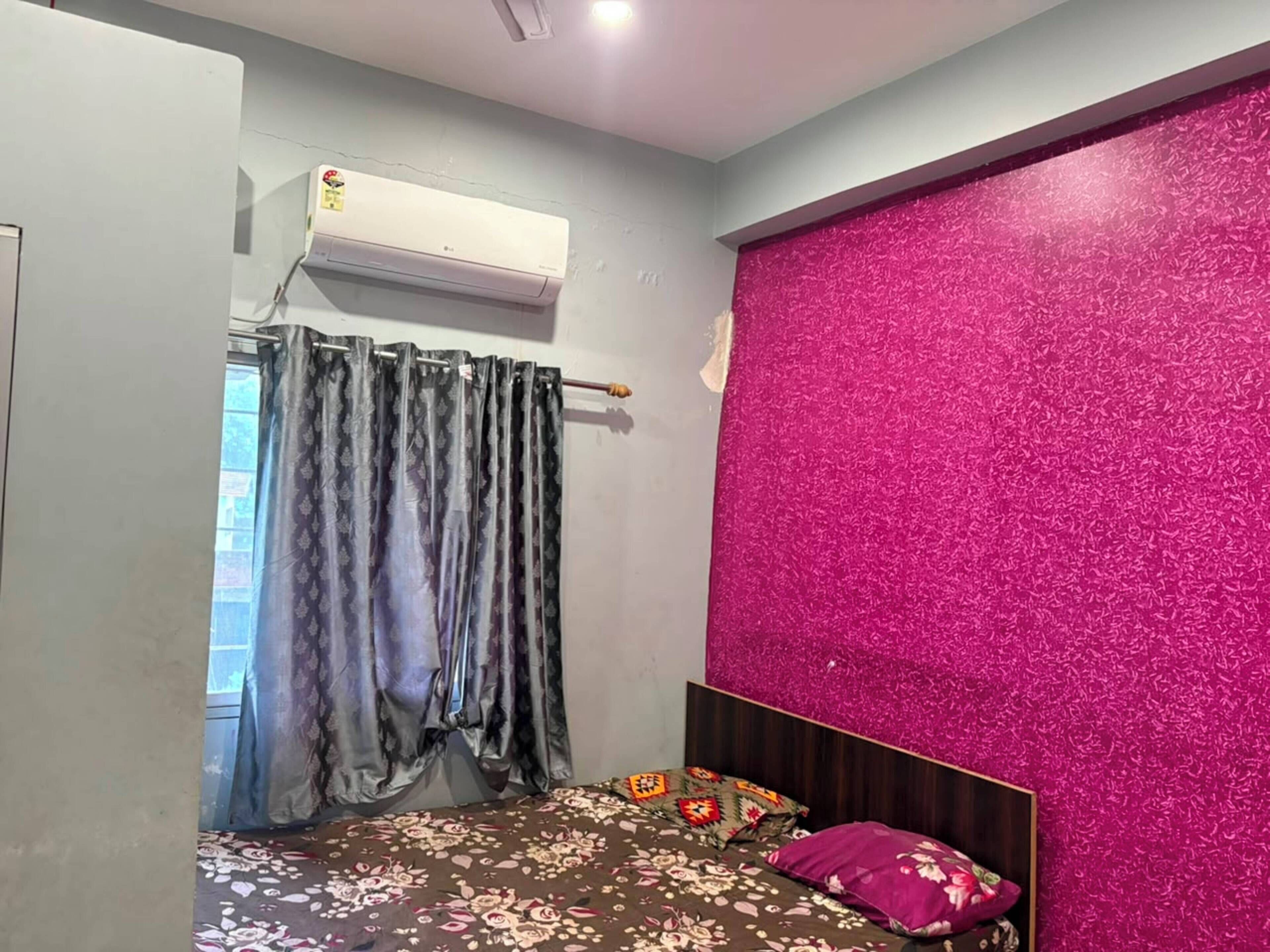 A bedroom with a bed, a curtain, an air conditioning unit, and a pink textured wall.