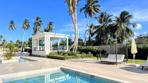 A pool area with lounge chairs, a covered seating area, and palm trees. - Serene Pool View Walk to Fun Beach Dine Shop (Punta Cana)