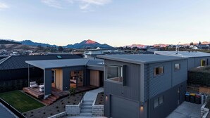Un immeuble résidentiel moderne doté d’un toit plat, d’un espace extérieur couvert avec un canapé, et offrant une vue sur les montagnes en arrière-plan.