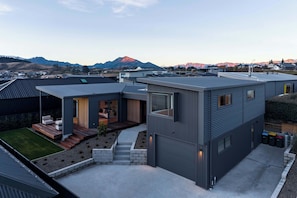 A modern residential building with a flat roof, a covered outdoor area with a sofa, and a view of mountains in the background. - Eliza's Escape with Mountain Views (Wānaka)