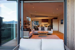 A modern interior with a living area, kitchen, and sliding glass doors leading to a balcony. - Eliza's Escape with Mountain Views (Wānaka)