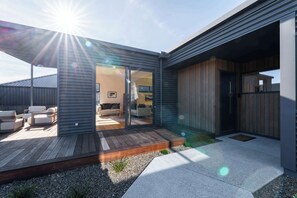 A modern house with a deck, a patio, and a visible interior with a sofa and a dining area. - Eliza's Escape with Mountain Views (Wānaka)