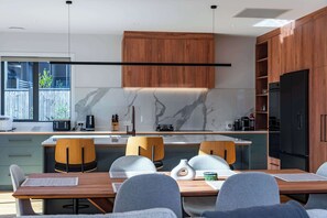 A modern kitchen with a marble backsplash, wooden cabinets, and a dining area with a table and chairs. - Eliza's Escape with Mountain Views (Wānaka)