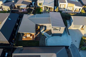 A modern residential building with a unique roof design, a covered outdoor seating area, and a well-maintained garden. - Eliza's Escape with Mountain Views (Wānaka)