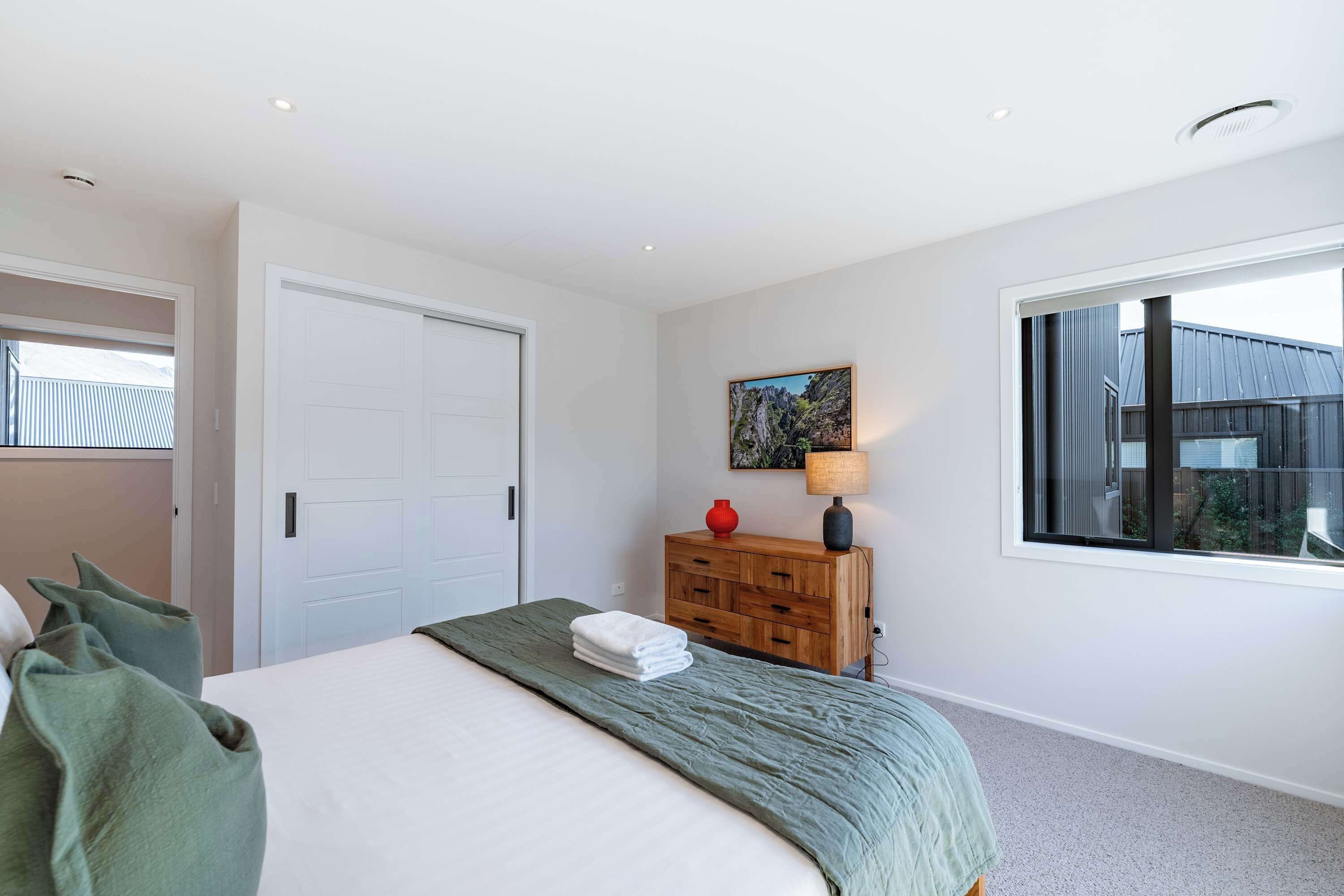 A bedroom with a bed, a dresser, a window, and a door.