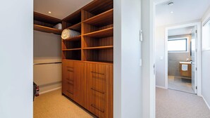 Un dressing avec des étagères et des tiroirs en bois, un sol recouvert de moquette et une porte donnant accès à une salle de bain.