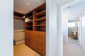 A walk-in closet with wooden shelving and drawers, carpeted floor, and a door leading to a bathroom. - Eliza's Escape with Mountain Views (Wānaka)
