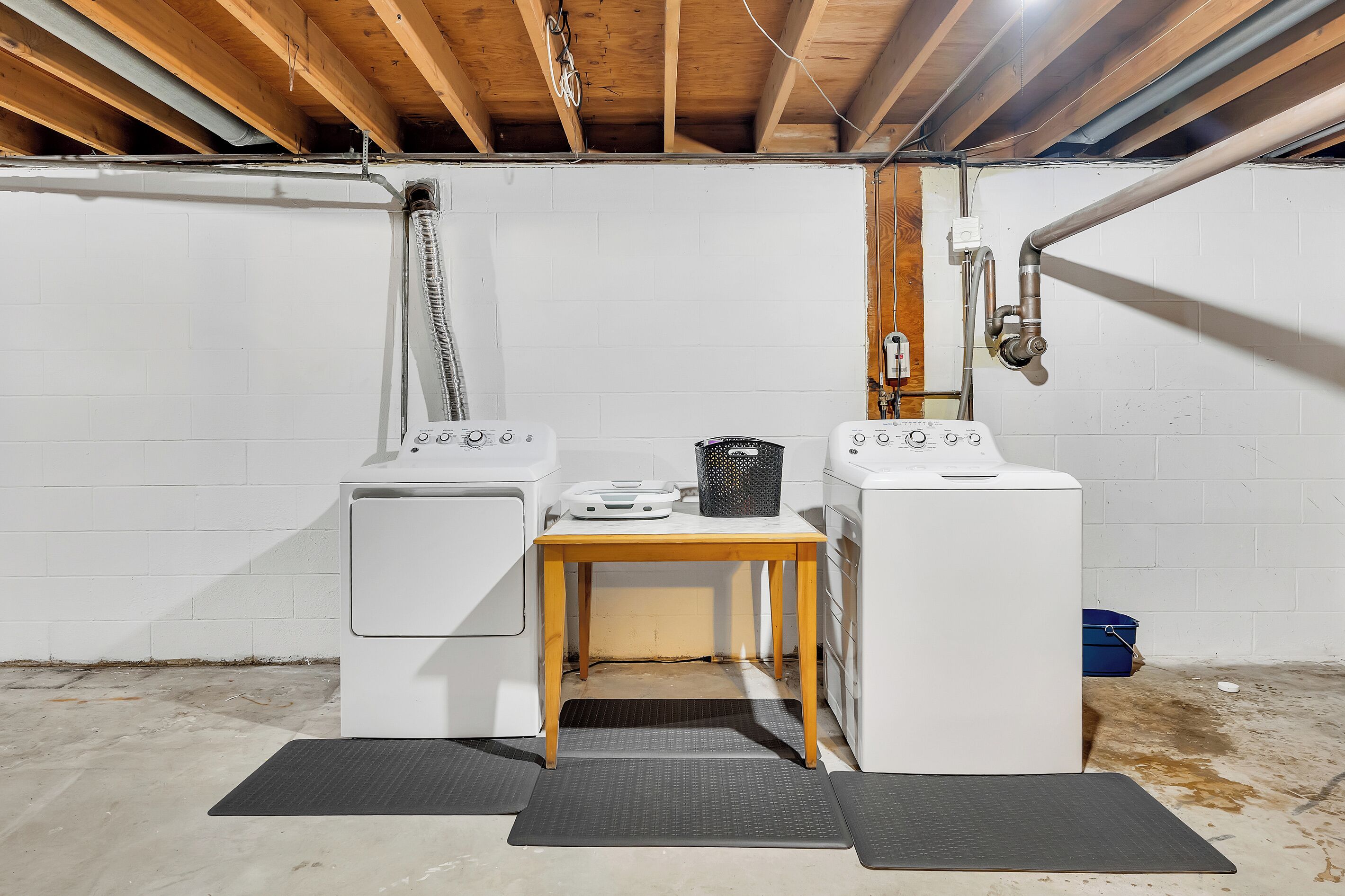 A laundry room with two washing machines, a table, and a trash bin.