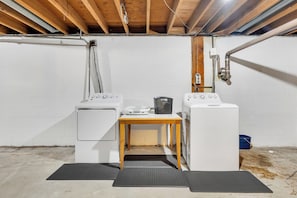 A laundry room with two washing machines, a table, and a trash bin.