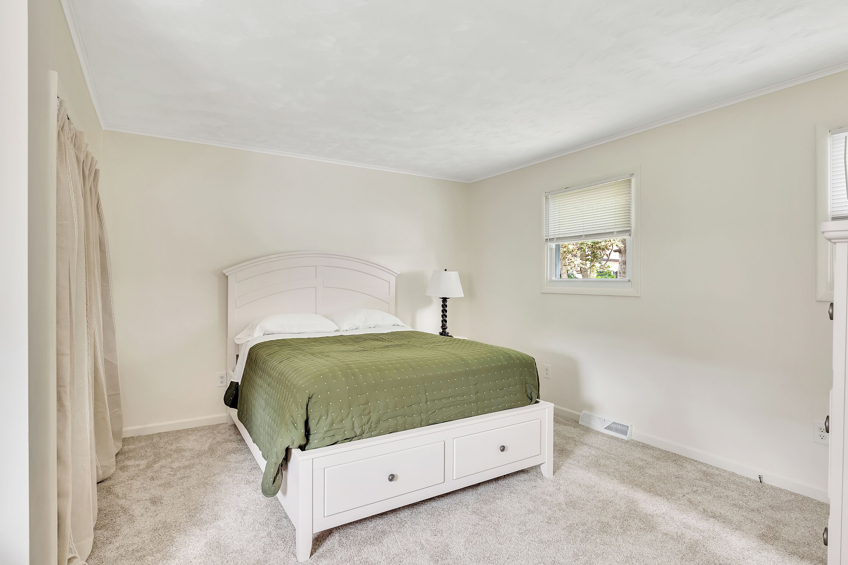 A bedroom with a bed, a nightstand, a window with blinds, and a door.