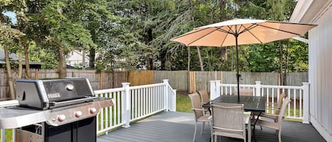Une terrasse extérieure équipée d’un barbecue, d’une table à manger, de chaises et d’un parasol.