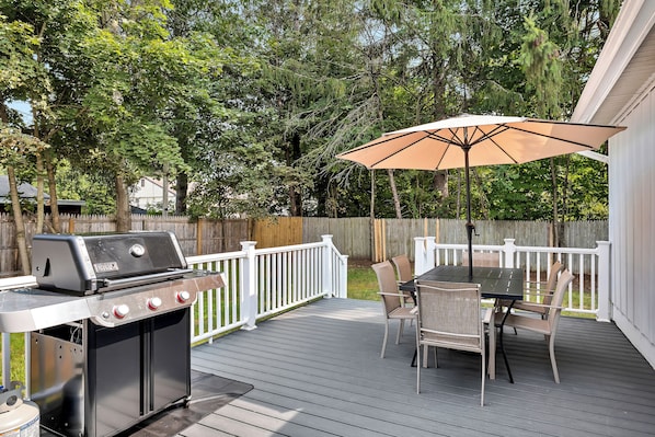 Een terras buiten, met een barbecue, eettafel, stoelen en een parasol.