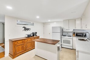 Una cucina moderna con mobili bianchi, un piano di lavoro in legno, una stufa in acciaio inossidabile, un forno integrato, un microonde e una macchina per il caffè.