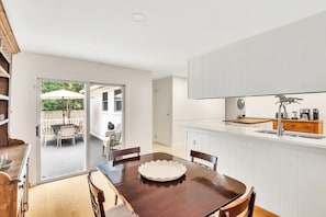 Een moderne keuken met witte kastjes, een houten eettafel en uitzicht op een terras.