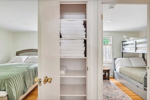 A bedroom with a bed, a closet with folded towels, and a window with curtains. - Oklahoma Breeze | Walk to Track & Downtown | 4BR + Pet Friendly (Saratoga Springs)