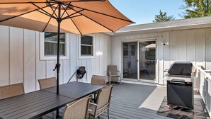 A patio with a table and chairs, a grill, and a covered area with an umbrella. - Oklahoma Breeze | Walk to Track & Downtown | 4BR + Pet Friendly (Saratoga Springs)