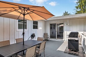 Een terras met een tafel, stoelen, een barbecue en een overdekt gedeelte met een parasol.