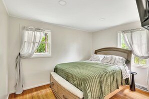 Een slaapkamer met een bed, een dressoir, een nachtkastje en een raam met gordijnen.