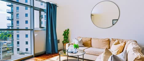 A modern living room with a sofa, a coffee table, and a large window with curtains.