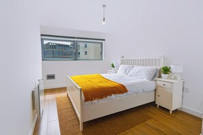 Un dormitorio con cama, mesitas de noche, ventana y radiador.
