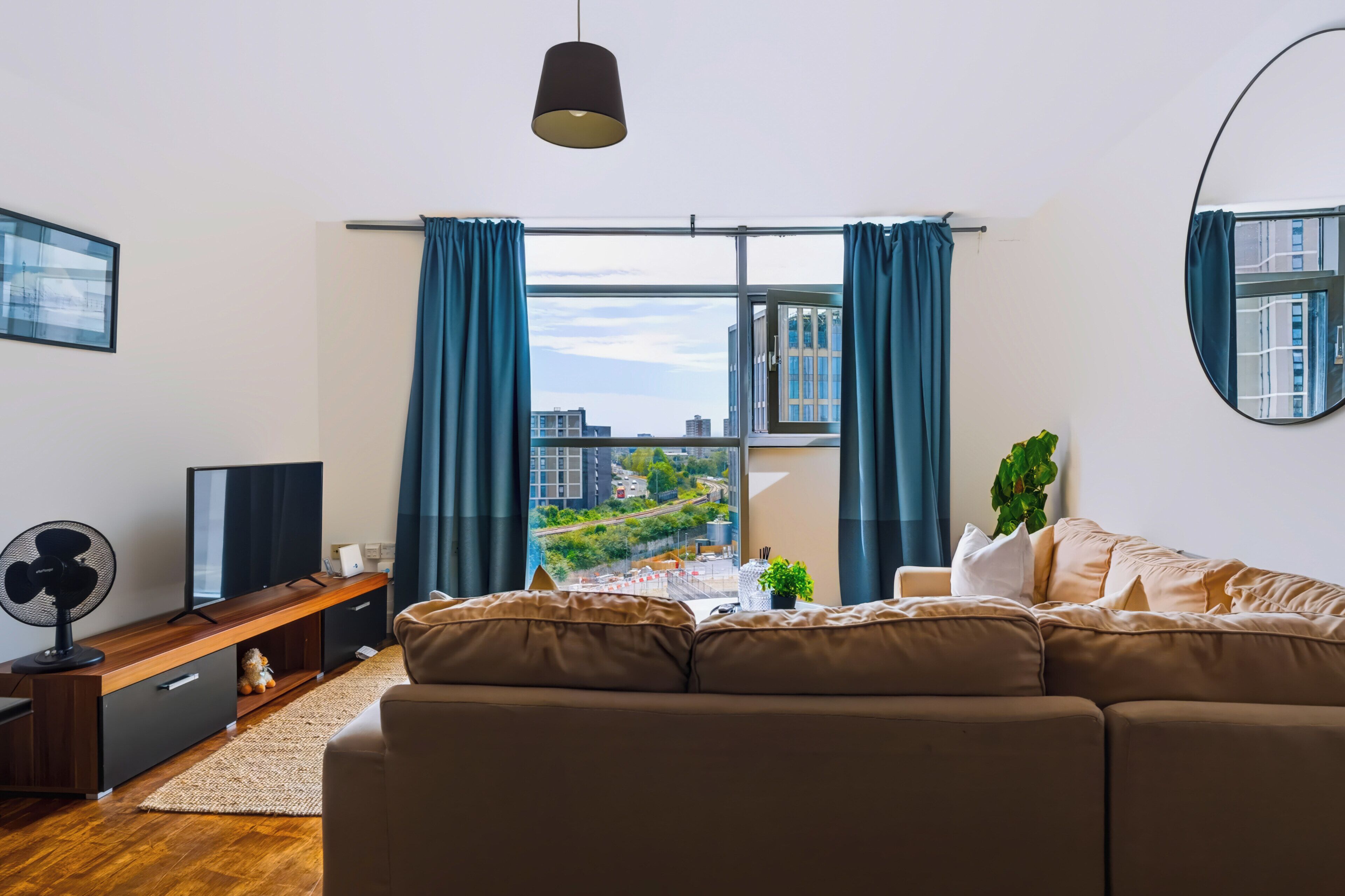 A modern living room with a large window, a sofa, a TV, and a fan.