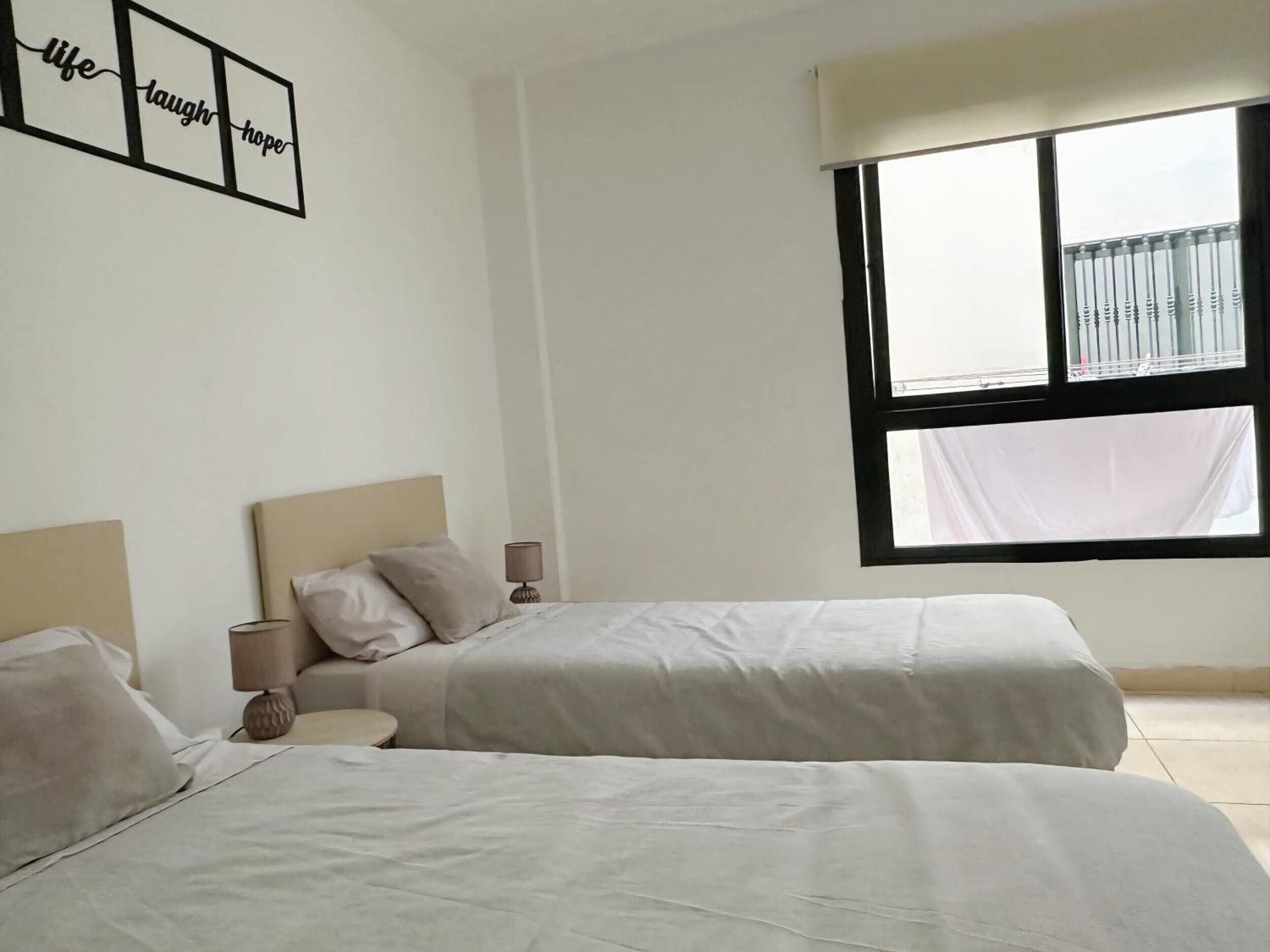 Un dormitorio con dos camas, una ventana con vistas y una pared con una cita inspiradora.