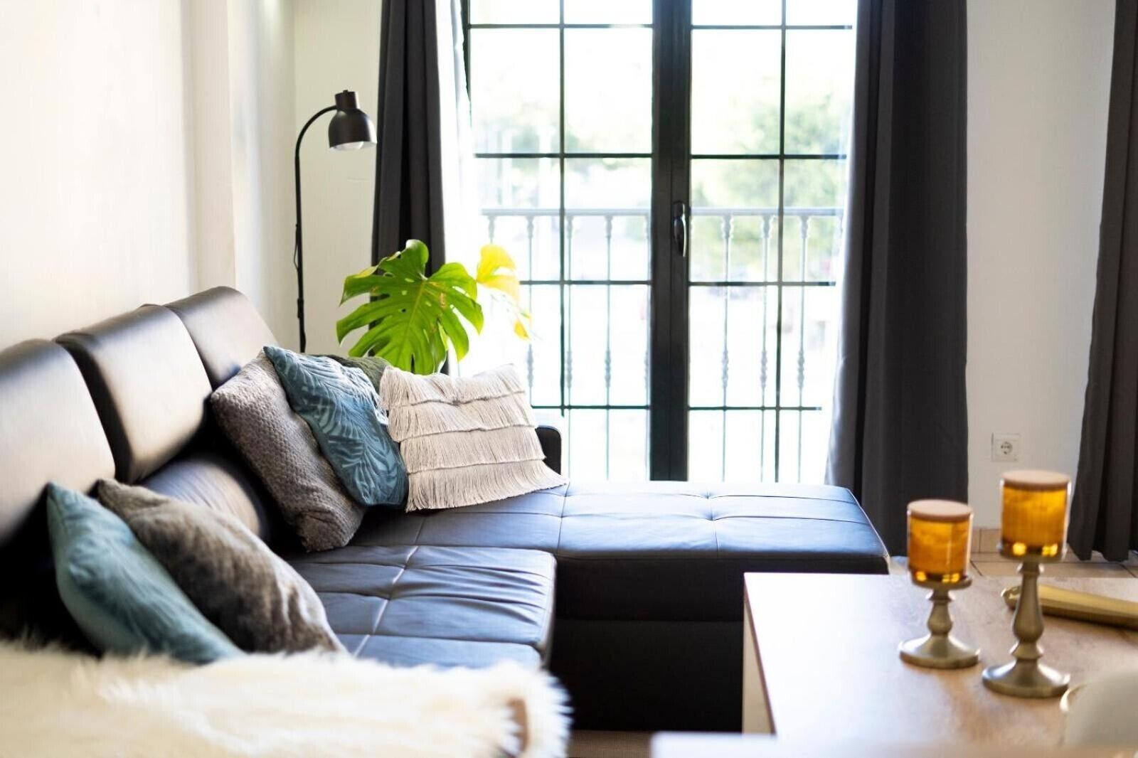 Ein modernes Wohnzimmer mit einem schwarzen Ledersofa, einer weißen, flauschigen Decke und einer Pflanze.