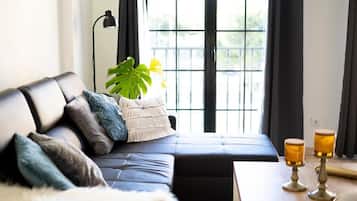 Ein modernes Wohnzimmer mit einem schwarzen Ledersofa, einer weißen, flauschigen Decke und einer Pflanze.