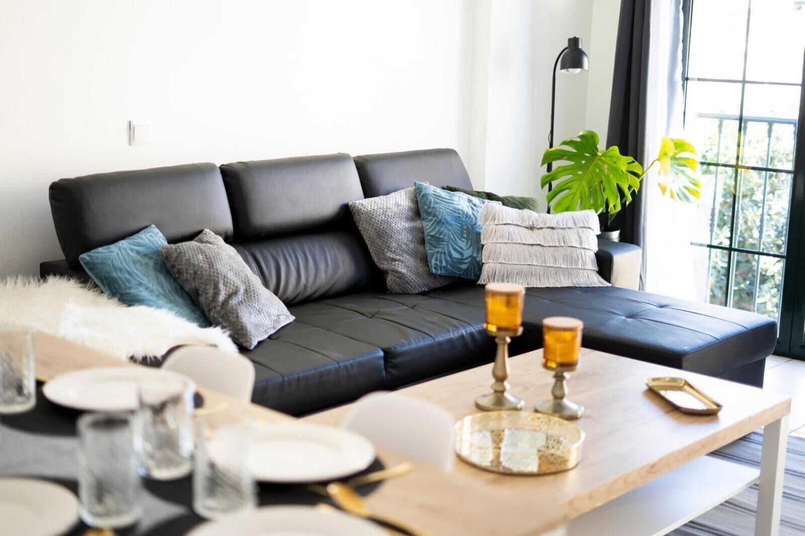 Un salón moderno con un sofá de cuero negro, una mesa de centro con cubierta de vidrio y un amplio ventanal con luz natural.