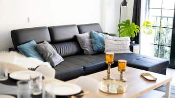 Un salón moderno con un sofá de cuero negro, una mesa de centro con cubierta de vidrio y un amplio ventanal con luz natural.