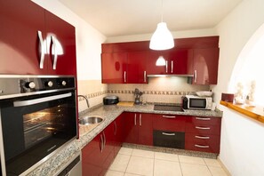 A compact kitchen with red cabinets, a built-in oven, a microwave, and a granite countertop. - Apartamento 'Estrella Del Sur Torremolinos' con vistas a la montaña, Wi-Fi y aire acondicionado (Torremolinos)