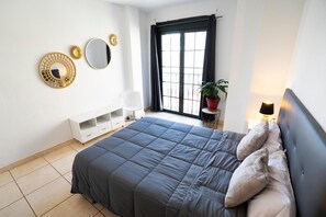 Quarto com uma cama, cômoda branca, espelho e janela com cortinas.