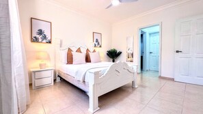 Ein Schlafzimmer mit Bett, Nachttischen, Deckenventilator und einer Tür.