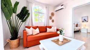 Ein Wohnzimmer mit einer Couch, einem Couchtisch, einer Topfpflanze und einer Wand-Klimaanlage.