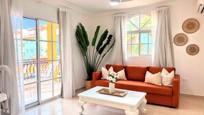 Ein Wohnzimmer mit einer Couch, einem Couchtisch und großen Fenstern mit Vorhängen.