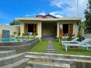 A two-story house with a swimming pool, outdoor seating, and a well-maintained lawn.