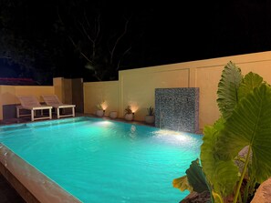 A swimming pool with a waterfall feature, surrounded by lounge chairs and potted plants.