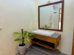 A bathroom with a white sink, wooden vanity, a large mirror, and a potted plant.