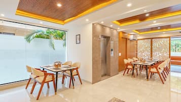 Un hall d’hôtel moderne comprenant un espace repas, un comptoir d’accueil et une grande fenêtre donnant sur des palmiers.
