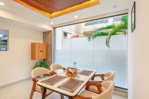 A modern dining area with a glass partition, wooden furniture, and a view of a building with a geometric facade.