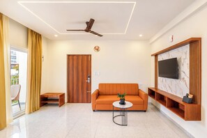 A modern living room with a ceiling fan, a wooden door, a sofa, a coffee table, and a TV mounted on the wall.